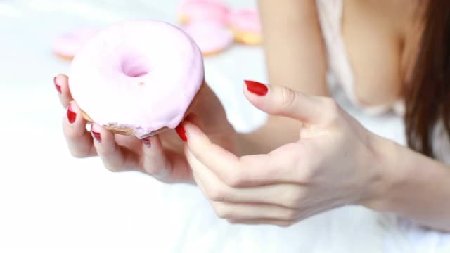 一个女人的特写是谁吃着彩色糖霜甜甜圈和微笑。视频素材