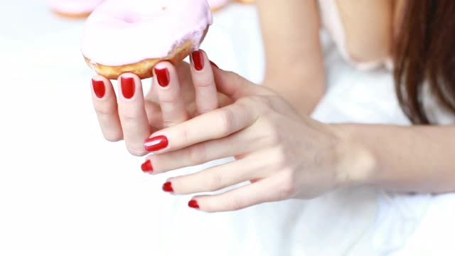 一个女人的特写是谁吃着彩色糖霜甜甜圈和微笑。视频素材