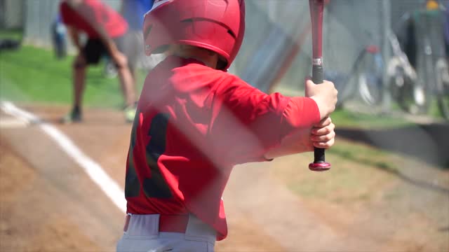 一个小男孩在打少年棒球联盟时击球。——慢动作视频下载