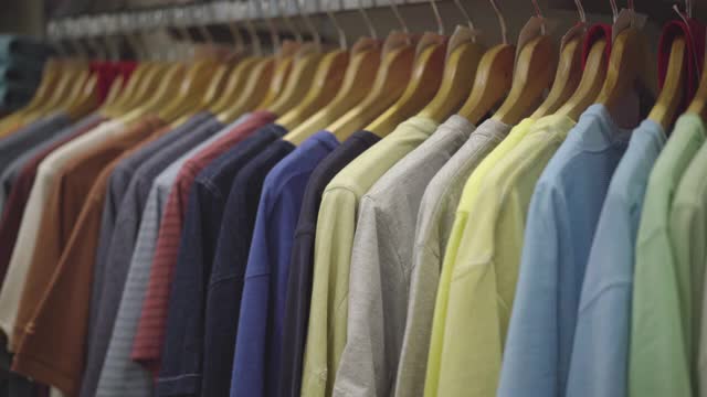 一排多色男t恤挂在服装店的衣架上。商场里衣架上的衣服。视频素材