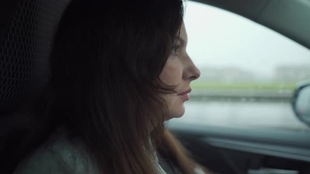 深褐色的女人，穿着大衣，坐在方向盘后面，在秋雨中驾驶汽车视频下载