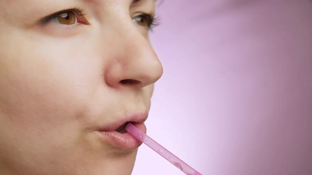 女人喝从一个粉红色的背景上的吸管，享受一个饮料近距离视频下载