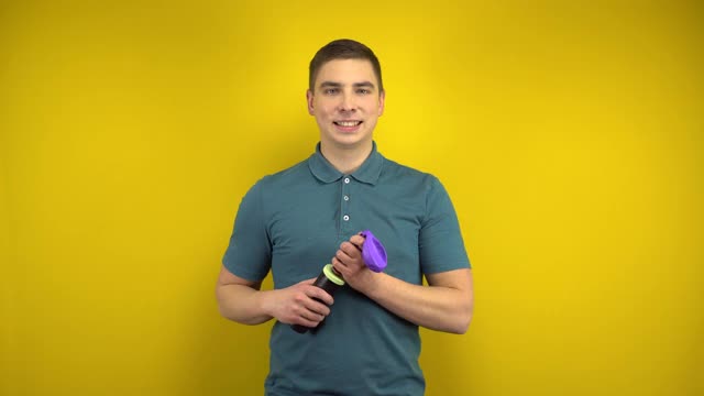 一个年轻人用黄色背景的打气筒给一个紫色的气球充气。穿绿色马球的男人。视频下载
