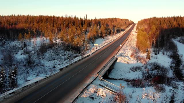 空中飞行在冬季森林，俯视图和道路下的阳光下日落视频素材