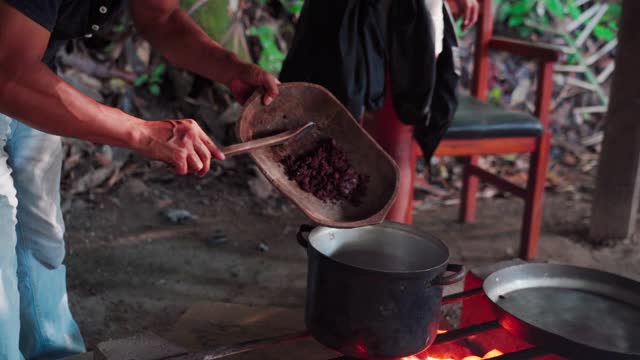 厄瓜多尔亚马逊地区，一名男子将木碗里的咖啡豆刮进火里视频下载