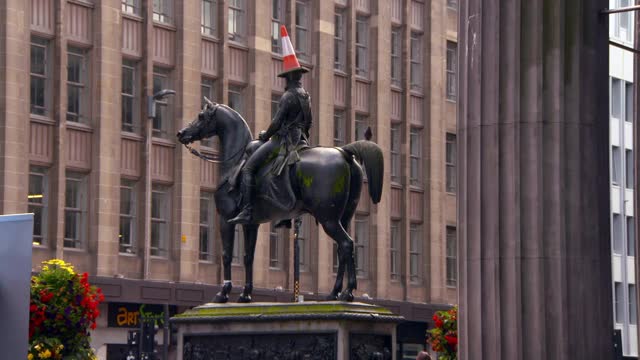 封锁:在熙熙攘攘的广场上有一个巨大的威灵顿骑马青铜雕像，头部被交通锥卡住了——苏格兰格拉斯哥视频下载