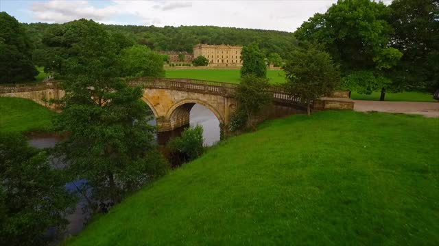 空中向前:石桥和宽阔的绿地通向庄严的乔治王朝伟大的家被森林包围-查兹沃斯，英国视频下载