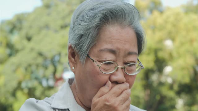 老年妇女在公园咳嗽。视频下载