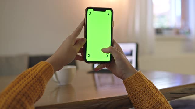 一个不认识的女人在家里使用绿屏色度键智能手机视频素材