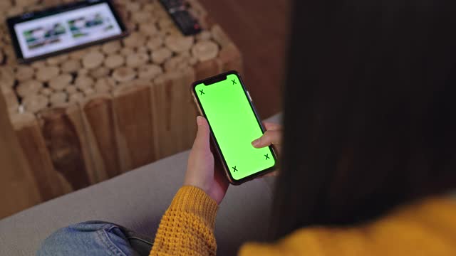 一名年轻女子坐在家里的沙发上使用彩色按键屏幕的智能手机视频素材