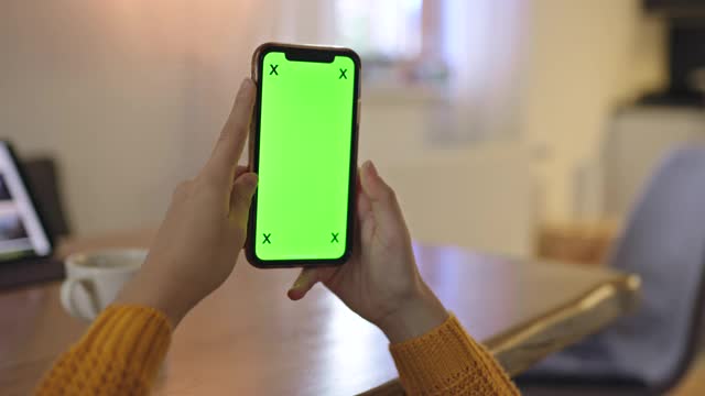 一个不认识的女人在家里使用绿屏色度键智能手机视频素材