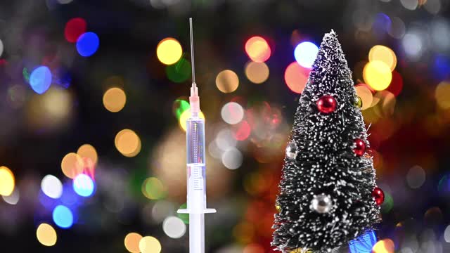 一个注射器靠近一个微型圣诞树的特写。圣诞彩灯的背景视频素材
