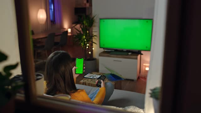 一名年轻女子用绿色色度键智能手机浏览电视节程表视频下载