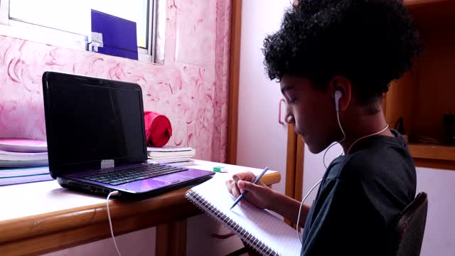 混血男孩在家里的笔记本上写笔记做作业视频素材