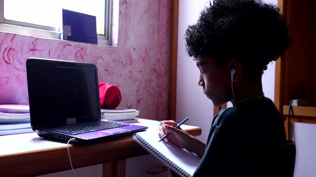混血男孩在家里的笔记本上写笔记做作业视频素材