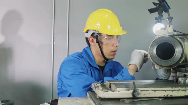 亚洲机械工人在铣床上工作。技术人员在操作机器时戴上防护眼镜和安全帽，以确保安全。这个人小心翼翼地工作以防危险。视频素材