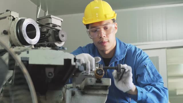 亚洲机械工人在铣床上工作。技术人员在操作机器时戴上防护眼镜和安全帽，以确保安全。这个人小心翼翼地工作，以防发生危险视频素材