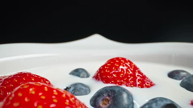 缓慢移动的近距离拍摄水果碗与草莓和下降的蓝莓和酸奶牛奶视频素材