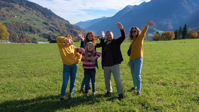 快乐的人们一家人站在奥地利阿尔卑斯山的绿色秋野上，在阳光明媚的十月日挥手致意视频下载