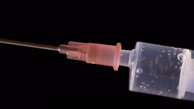 注射:使用注射器时的特写。透明液体(疫苗)正从注射器中流出。黑色背景。视频下载