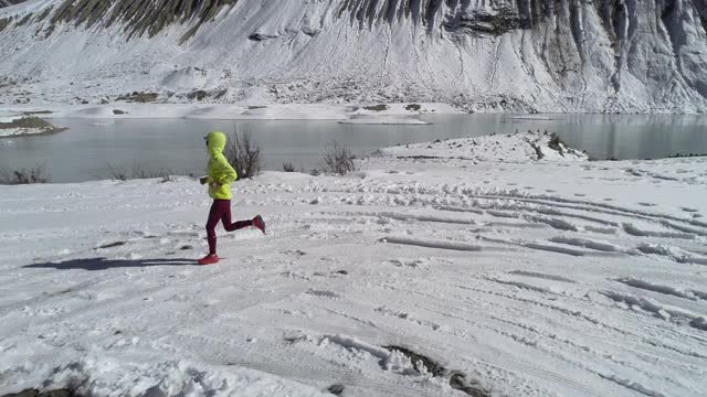 女子越野跑越野跑在冬天的自然，鸟瞰无人机镜头，慢镜头视频素材