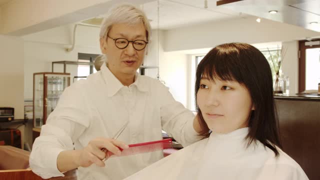 日本一名男性美发师正在为一名日本女性做头发和化妆，同时与美发师聊天视频下载