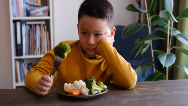 孩子对不得不吃蔬菜很不高兴。他的盘子里有许多蔬菜。他讨厌蔬菜。视频下载