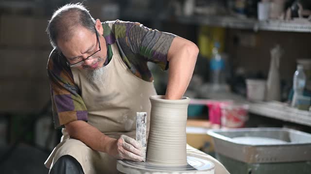 亚洲华人高级泥塑艺术家在他的工作室与纺织陶轮工作视频素材