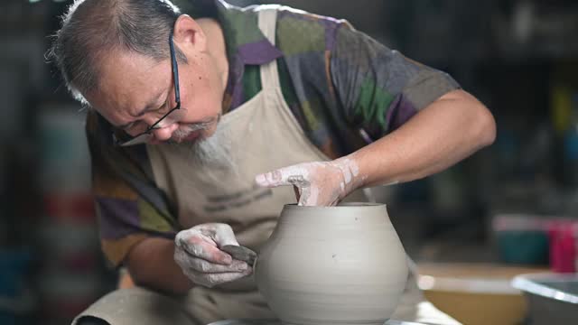亚洲华人高级泥塑艺术家在他的工作室与纺织陶轮工作视频下载