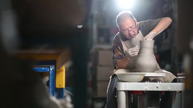 亚洲华人高级泥塑艺术家工作在他的工作室与纺织陶轮视频素材
