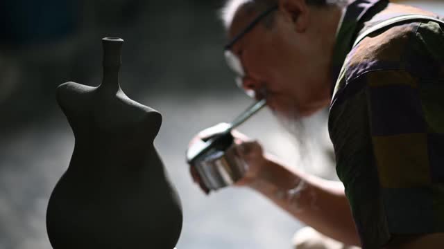 亚洲华人高级泥塑艺术家在雕塑家身上吹颜料，在他的工作室里用纺纱陶轮工作视频素材