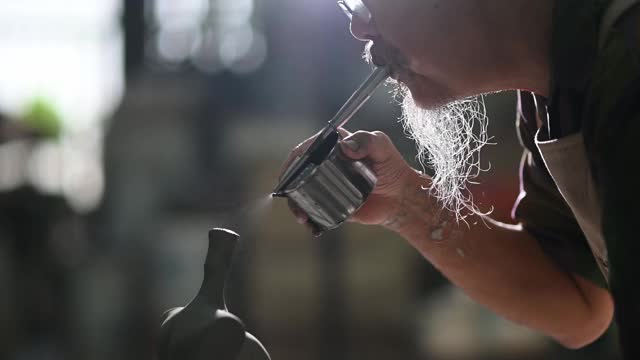 亚洲华人高级泥塑艺术家在雕塑家身上吹颜料，在他的工作室里用纺纱陶轮工作视频素材
