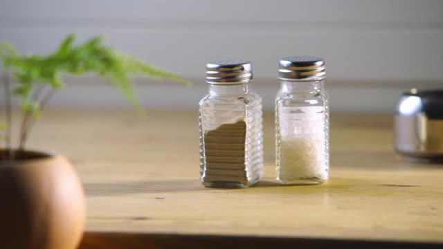 木制桌面上放着一对简单的玻璃盐瓶和胡椒瓶。视频素材