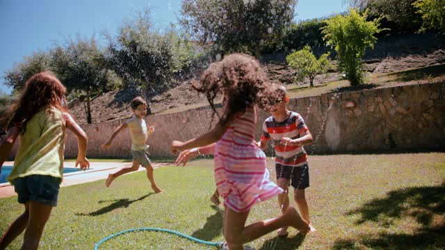 一群孩子在花园里玩耍，跳过洒水器视频素材