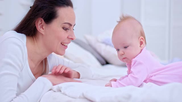 肖像，一个年轻美丽的母亲正在和她的新生儿说话，并对她微笑。新生的婴儿躺在轻便的床上，看着她的母亲，快乐的母亲。4 k, ProRes视频素材