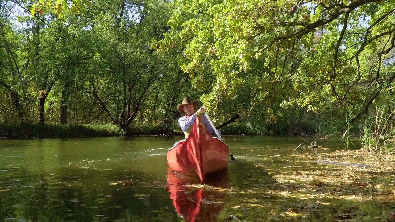 一只独木舟上的牛仔漂在森林中的河上视频下载