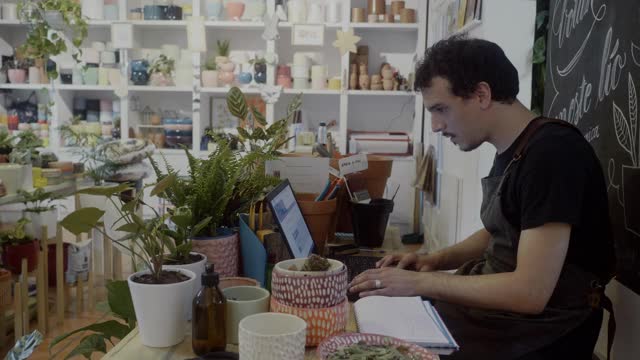 在他的植物精品店里用笔记本电脑工作的小企业主视频素材