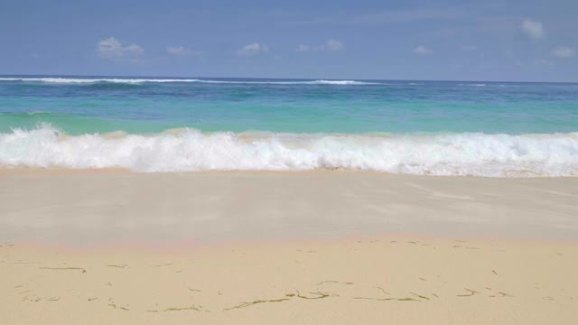 一个手持式的镜头，从一个巨大的美丽的蓝色海浪和岩石在缓慢的动作热带沙滩上行走视频下载