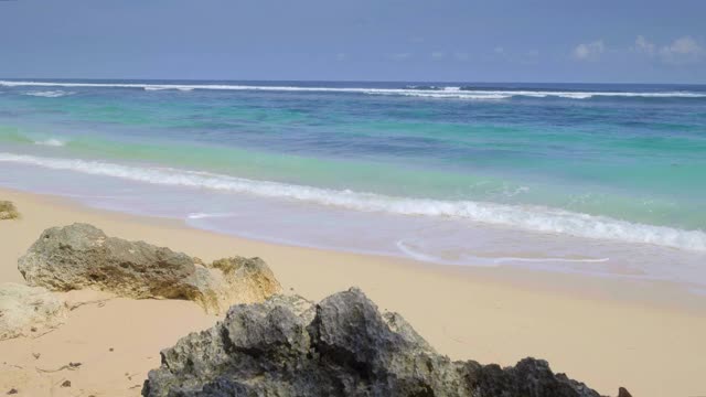 一个缓慢的热带海滩与岩石和海浪与泡沫的手持式拍摄视频下载