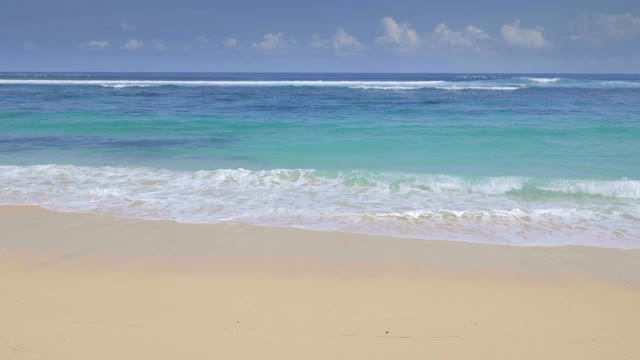 一个热带沙滩和岩石的全景镜头与彩色的蓝色的水和海浪在慢动作拍摄视频下载