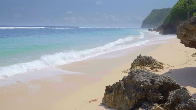 一个手持拍摄在热带海滩与岩石和树木与大波浪和雾的慢动作视频下载