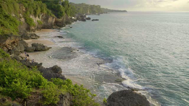 在热带岛屿上温暖的日落期间，绿色岩石沙滩上的人和大浪的慢动作视频下载