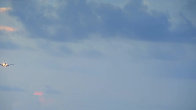 一架头灯小喷气式飞机在日落时分降落，天空中有蓝色和黄色的云视频下载