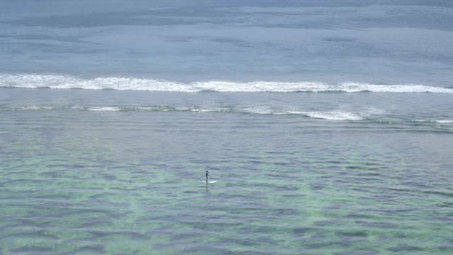 一个年轻的女人是划桨在清澈透明的水在低潮与小海浪附近的热带海滩礁石视频下载