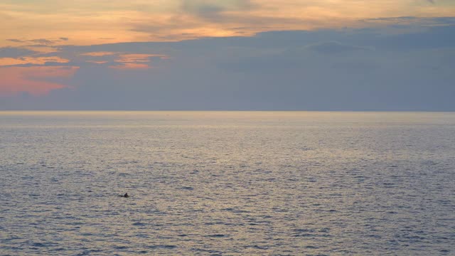 皮划艇人的剪影在海上与小波浪日落与乌云和黄色的天空视频下载