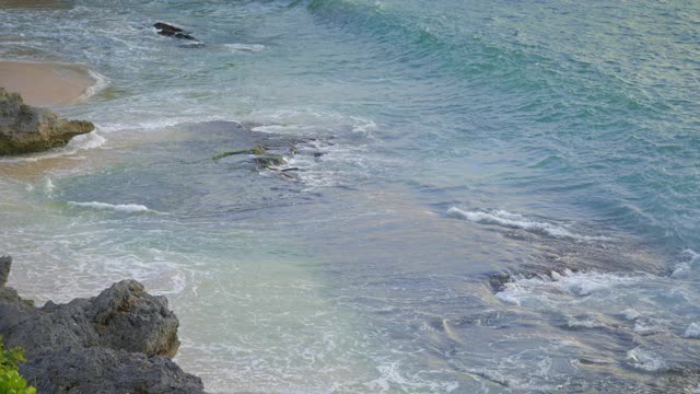 近距离拍摄的岩石在热带沙滩上的高潮汐与高泡沫波浪在温暖的日落视频下载