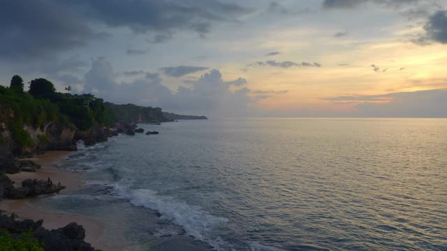巴厘岛上的热带海滩，人们在岩石上，在黑暗的日落天空中掀起巨浪视频下载