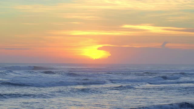 在巴厘岛美丽的黄色和紫色日落期间，海面和冲浪者在温暖的海洋与大浪潮游泳的全景视频下载