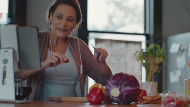 一个外向的女人一边在厨房里切蔬菜一边跳舞，一边和朋友视频聊天视频下载
