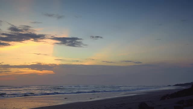 美丽的日落与蓝色和红色的天空在海滩上与黑色的沙子和波浪与雾视频下载